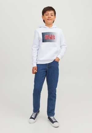 Witte hooded sweatshirt met een grafische print in rood en zwart, gecombineerd met blauwe denim jeans en marineblauwe sneakers met witte zolen.