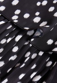 Tessuto nero con macchie irregolari bianche, caratterizzato da pieghe e un design a strati nella parte superiore, texture liscia e caduta morbida.