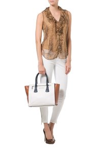 Mujer con blusa sin mangas de estampado de serpiente marrón con volantes y pantalones blancos, sosteniendo un gran bolso blanco, marrón y negro, y usando tacones marrones.
