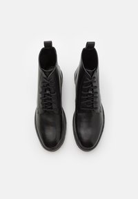 Botines de cuero negro con un acabado suave, punta redondeada y cordones. Presenta una lengüeta en la parte trasera y acentos cosidos a lo largo de la suela.