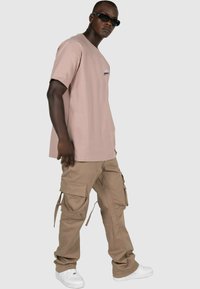 Lyserød bomulds T-shirt med korte ærmer, parret med beige cargo bukser med flere lommer og snore. Båret med hvide sneakers.