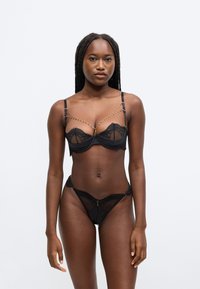 Ensemble de lingerie en dentelle noire comprenant un soutien-gorge à armatures, bretelles réglables et accents en chaîne, assorti à un string.