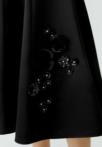 Jupe noire avec des appliqués floraux brillants regroupés, mettant en avant de petits centres en strass, portée au-dessus du genou.