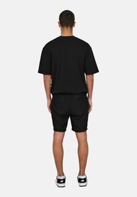 Camiseta negra de manga corta, combinada con pantalones cortos negros. La tela parece suave; diseño minimalista sin patrones visibles. Zapatillas negras.