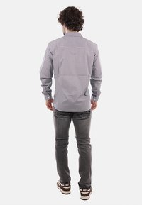 Camicia a maniche lunghe con una piccola stampa geometrica in blu navy e bianco, con colletto a bottone e maniche arrotolate, abbinata a jeans grigi.