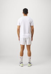 White short-sleeve polo and white shorts, both made of lightweight fabric. Model wears white socks and sneakers with colorful accents.
