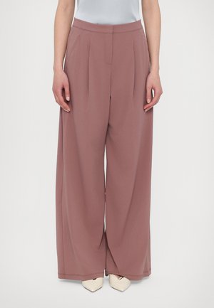 Wide-leg trousers in soft, dusty rose fabric. Features pleats, side pockets, and a smooth waistband. Paired with pointed, cream-colored shoes.