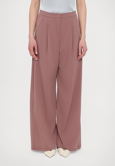 Pantalons larges en tissu rose poussiéreux doux. Comprend des plis, des poches latérales et une taille lisse. Associé à des chaussures pointues de couleur crème.