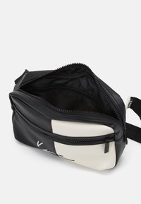 Borsa a tracolla piccola in bianco e nero con due scomparti con cerniera, uno parzialmente aperto, che mostra la fodera interna nera.