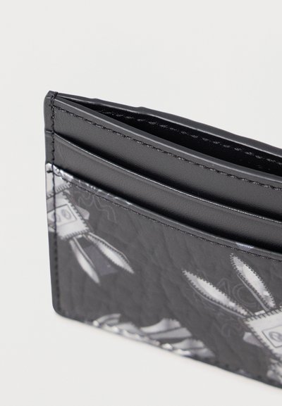 Tarjetero de cuero negro con patrón en relieve, que cuenta con dos ranuras para tarjetas y un acabado texturizado. Los bordes son suaves con costuras precisas.