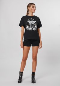 Musthave musträbaline T-särk mustast puuvillast, millel on valge liblikas ja lilleline graafika. Koos mustade lühikesed pükste ja naglikannaga saapadega, millel on nurgelised kaunistused.