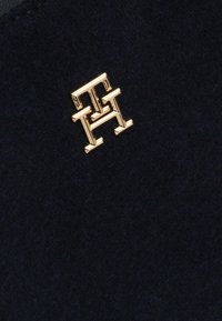 Tessuto di lana blu navy con un accento in logo metallico dorato con iniziali stilizzate, superficie liscia e linee pulite.