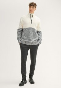 Lange mouwen trui in crèmewit en grijs breiwerk met een hoge kraag en rits, gecombineerd met donkergrijze slim-fit broek en zwarte veterschoenen.