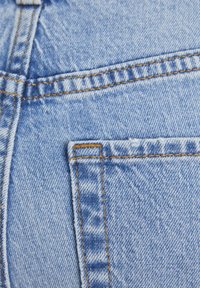 Jeans in denim azzurro leggero presentano una tasca posteriore visibile con cuciture arancioni. Il tessuto mostra una consistenza morbida e una finitura leggermente sbiadita.