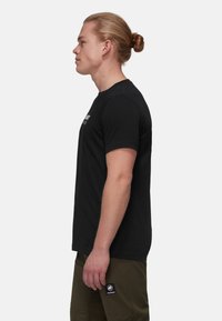 T-shirt en coton noir à manches courtes, col rond, avec un design de texte blanc sur la poitrine. Le t-shirt est ajusté, avec une texture lisse.