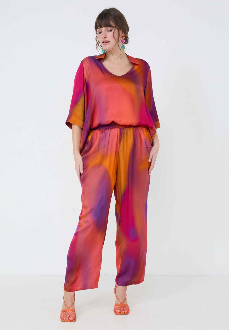 Zijden jumpsuit met een V-hals, losse pasvorm en een levendig verloop van oranje, roze en paarse tinten; gecombineerd met oranje sandaaltjes met bandjes.
