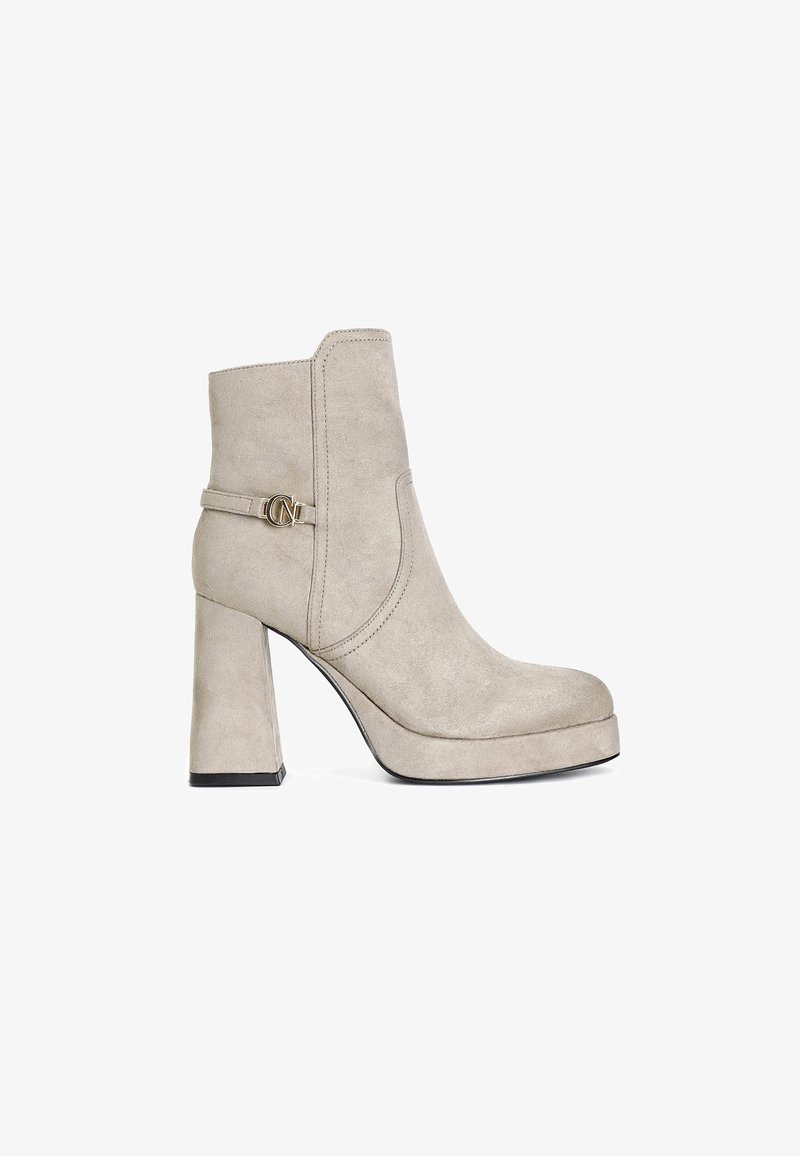 Beige suède enkellaarsjes met een vierkante hak en platform. Voorzien van een zijband met een metalen accent. Gladde textuur en ronde teenvorm.