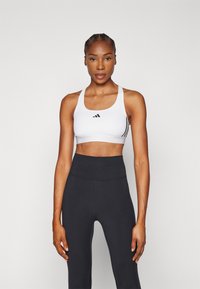 Witte sport-bh met zwarte accenten en drie strepen aan de zijkant, gecombineerd met hoge zwarte leggings. Zacht, rekbaar materiaal.
