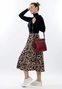 Leopard-print skirt, black fitted top, burgundy crossbody bag with tassel, and white sneakers. Smooth fabric, A-line shape, mid-calf length.