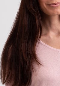 Dlouhé, rovné hnědé vlasy splývající přes měkký, světle růžový pletený svetr s kulatým výstřihem. Hladká textura s jemným žebrováním.