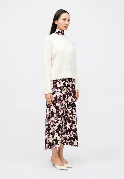 Krémový pletený sveter s okrúhlym výstrihom, skombinovaný s čiernymi kvetovanými midi šatami v odtieňoch ružovej. Modelka má na nohách biele špicaté baleríny.