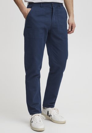 Pantalones de algodón azul marino con corte ajustado, que cuentan con dos bolsillos laterales y un diseño de pierna recta, combinados con zapatillas blancas.