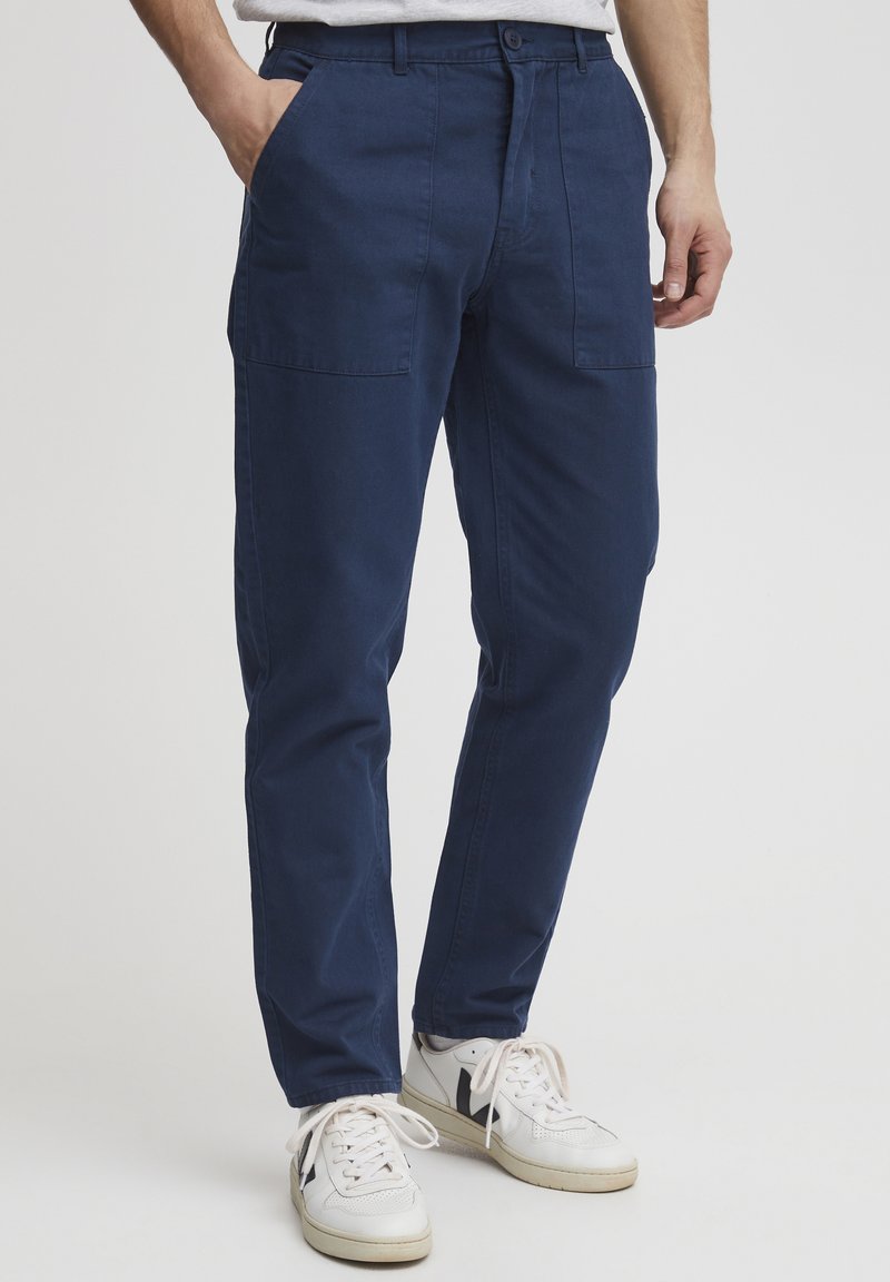 Pantalones de algodón azul marino con corte ajustado, que cuentan con dos bolsillos laterales y un diseño de pierna recta, combinados con zapatillas blancas.