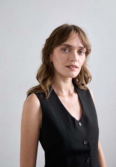 Svart ermeløs kjole med dyp V-hals, fem knapper foran og et glatt, teksturert stoff. Enkel design uten mønstre.