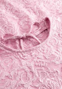 Pink lace fabric with textured floral patterns, featuring a round neckline and a bow detail at the back. Soft and delicate appearance.