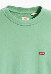 T-shirt a girocollo in cotone verde chiaro con maniche corte e una piccola toppa con il logo Levi's rosso sul petto a sinistra. Texture liscia.