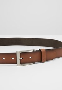Ceinture en cuir marron avec une texture lisse, dotée d'une boucle en métal argenté et de plusieurs trous d'ajustement le long de la sangle.