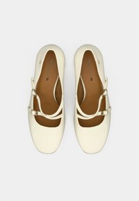 Λευκά επίπεδα παπούτσια με στρογγυλή μύτη, δύο λεπτές λωρίδες με αγκράφες κατά μήκος του ποδιού και λεία υφή τύπου δέρματος.