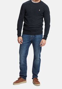 Granatowy sweter z okrągłym dekoltem wykonany z dzianiny, zestawiony z jasnoniebieskimi jeansami i brązowymi zamszowymi trampkami z beżowymi podeszwami.