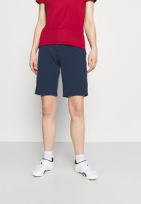 Námořnické modré šortky s rovný střihem, vyrobené z hladké látky. V kombinaci s červeným tričkem a bílými sportovními botami. Jednoduchý, funkční design.