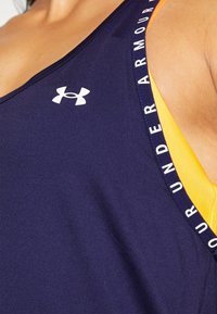 Námořnický sportovní top s širokými ramínky a bílým logem Under Armour, se žlutým akcentem na vnitřní straně a potiskem textu.