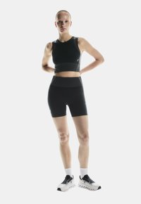 Schwarzes Sport-Tanktop und hoch taillierte Shorts aus dehnbarem Material mit einer figurschmeichelnden Passform. Getragen mit weißen und schwarzen Turnschuhen.