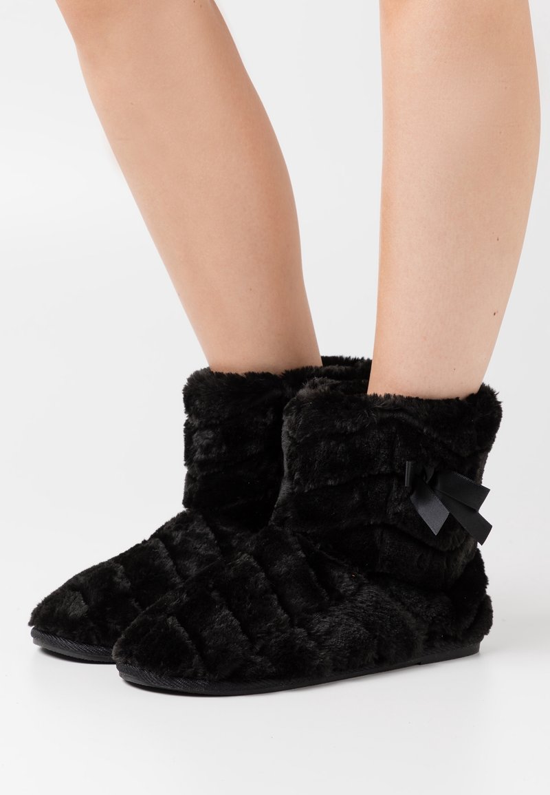 Schwarze Stiefel aus Kunstfell mit einem gesteppten Muster, ausgestattet mit einer seitlichen Schleifen-Akzentuierung und einer flexiblen Sohle für zusätzlichen Komfort.