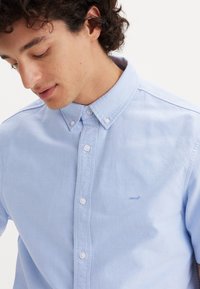 Lyseblå skjorte med knapper lavet af bomuld, med klassisk krave og subtilt broderet Levi's-logo på brystet. Glat tekstur.