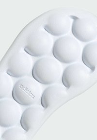 Suela de zapato de goma blanca con un patrón de burbujas texturizado, que presenta un logo "adidas" grabado cerca de la parte inferior. Acabado suave y bordes redondeados.