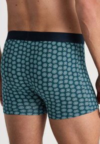 Boxershorts in een donker teal stof, met een hexagonaal patroon in lichtblauw en wit. Elastische tailleband in effen zwart.