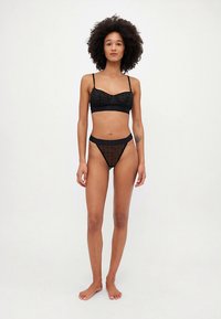 Ensemble de lingerie noire en tissu doux et transparent à motif à pois, avec bretelles réglables et coupe ajustée. Comprend un bralette et un slip assortis.