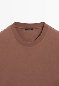 Bruin T-shirt met een ronde hals, gemaakt van lichtgewicht stof. Heeft een geribde kraag en een label aan de binnenkant van de halslijn.