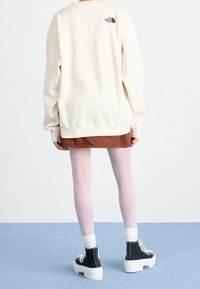 Sweat-shirt couleur crème avec un logo au dos, accompagné d'une jupe marron et de collants roses, ainsi que de bottines à plateformes noires avec des semelles blanches.