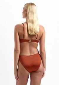 Bikini color ruggine con texture a coste, dotato di sottili spalline regolabili e di una chiusura dorata sul retro. Design della parte inferiore a vita alta.