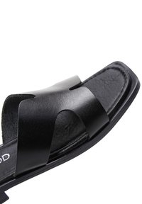 Schwarze Leder-Sandale mit zwei breiten Querriemen und einem strukturierten Fußbett. Die Sohle ist flach mit einem leicht erhöhten Rand.