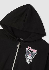 Felpa nera con zip argentata e una piccola grafica del personaggio Kuromi in rosa, bianco e grigio sul lato sinistro del davanti.