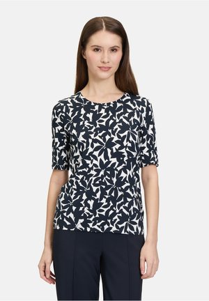 Haut à manches courtes bleu marine et blanc avec un motif de feuilles, col rond et coupe décontractée, fabriqué à partir d'un tissu lisse.