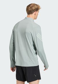 Mand set bagfra iført en lysegrå langærmet sportstrøje med hul til tommelfingrene og sorte shorts med Climacool-logo.