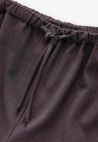 Pantaloni con cintura a cordoncino in tessuto viola intenso, caratterizzati da una superficie morbida, fascia elastica in vita e un dettaglio a nodo.