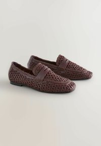 Mocassins en cuir bourgogne tressé avec une semelle plate noire et une lanière décorative à l'avant, présentant des détails texturés tout au long.